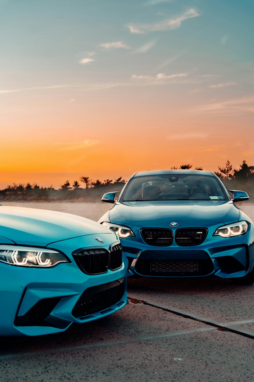 a couple of cars parked on a road with a sunset in the background