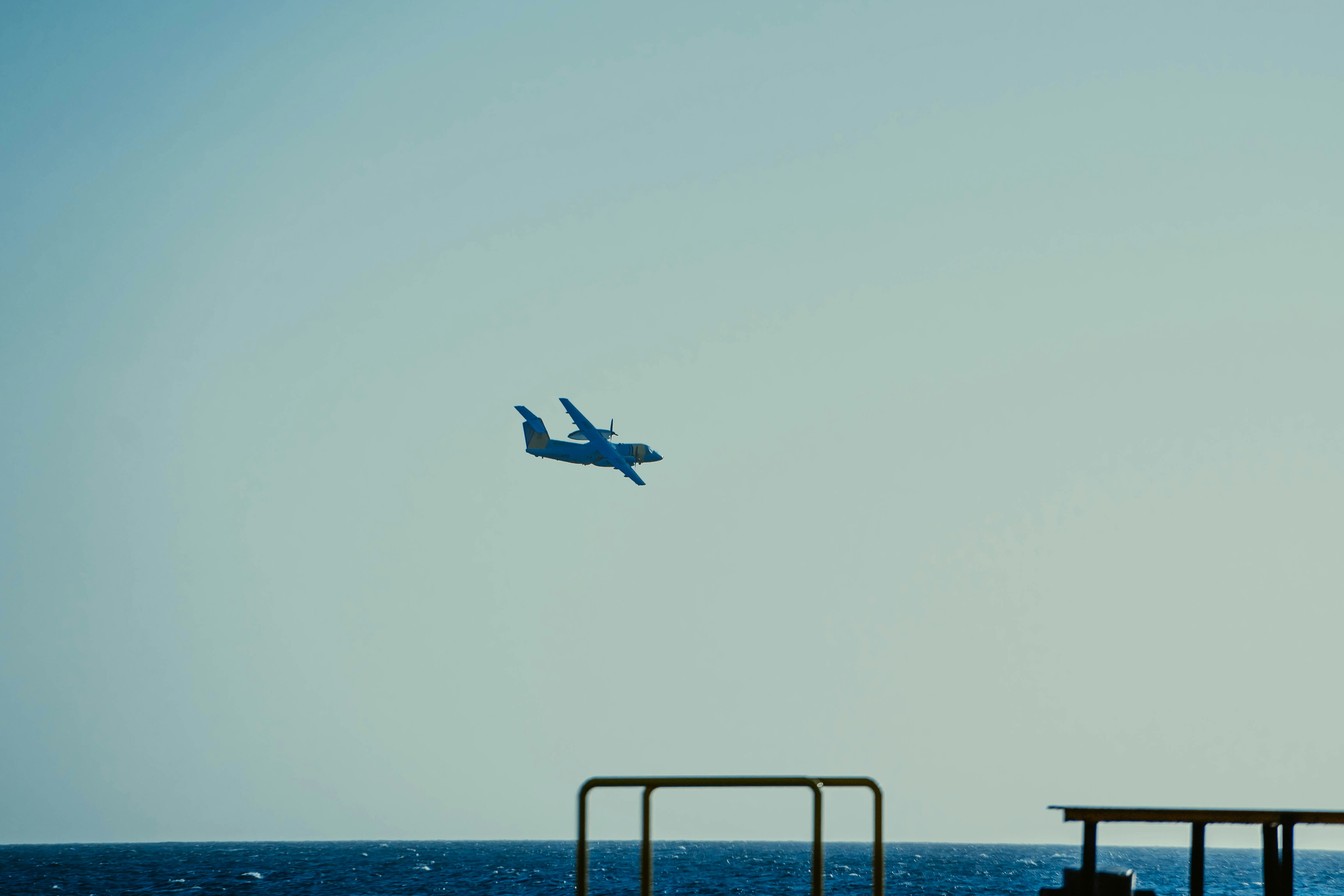 a blue airplane flying over a pier