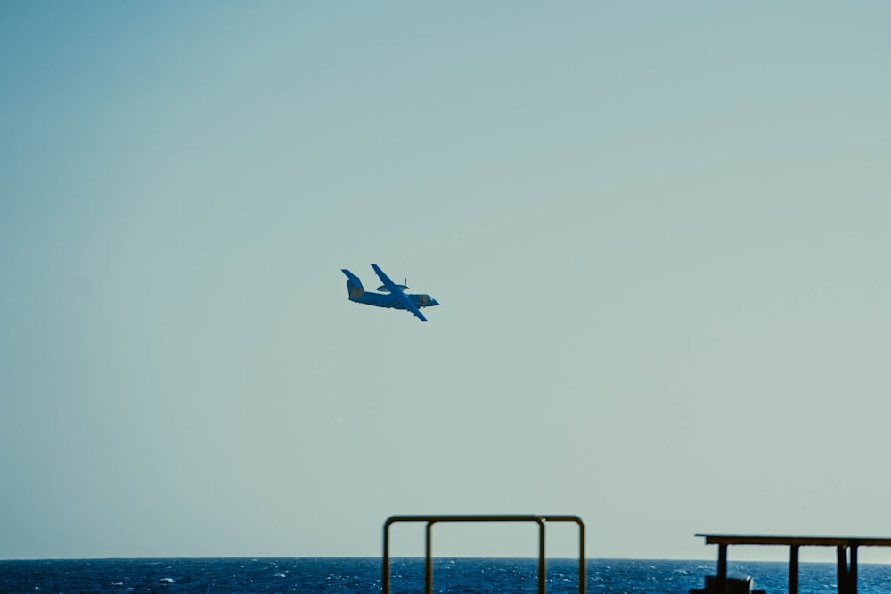 a blue airplane flying over a pier