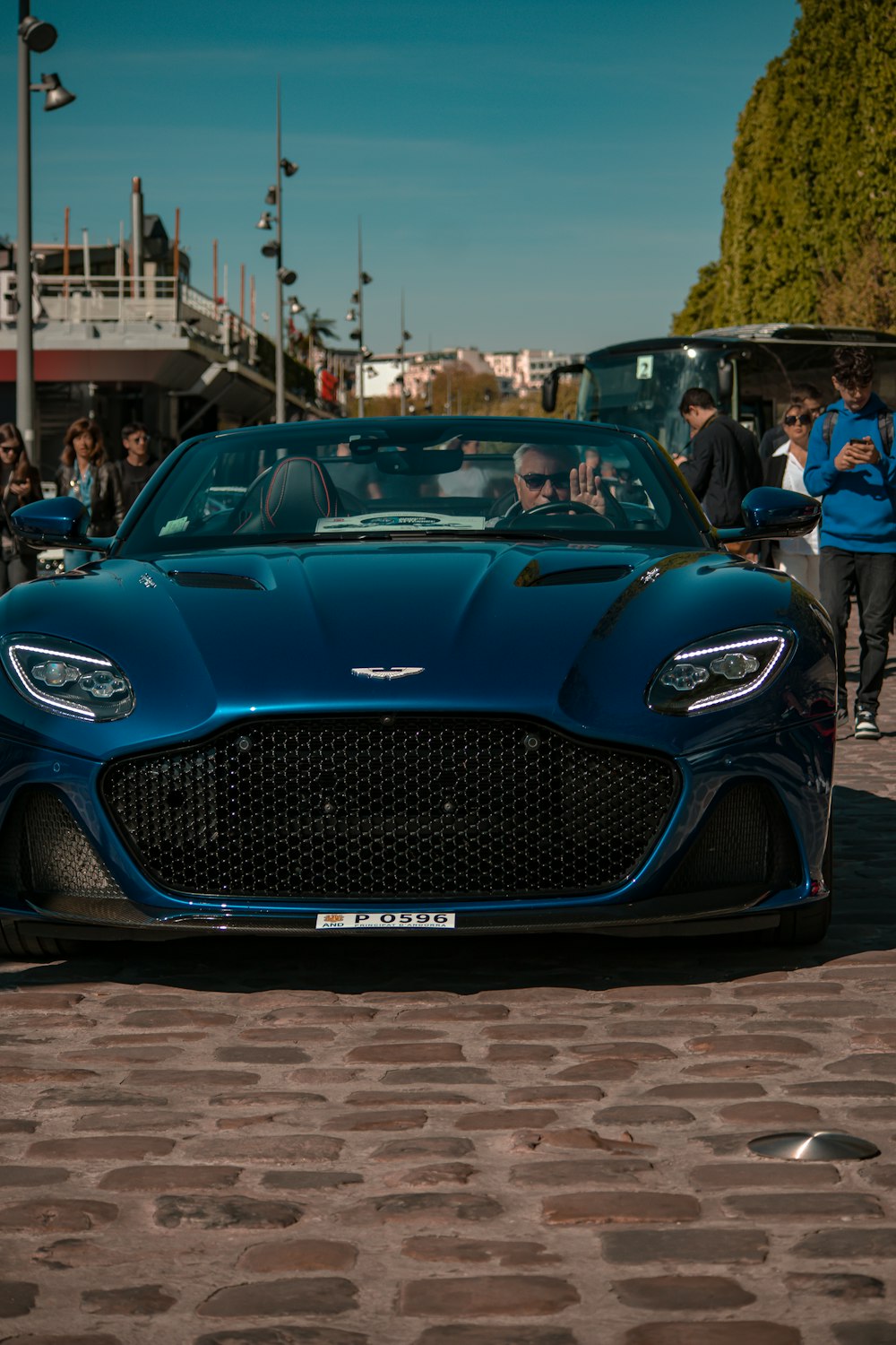 a blue car parked on a brick road with people standing around