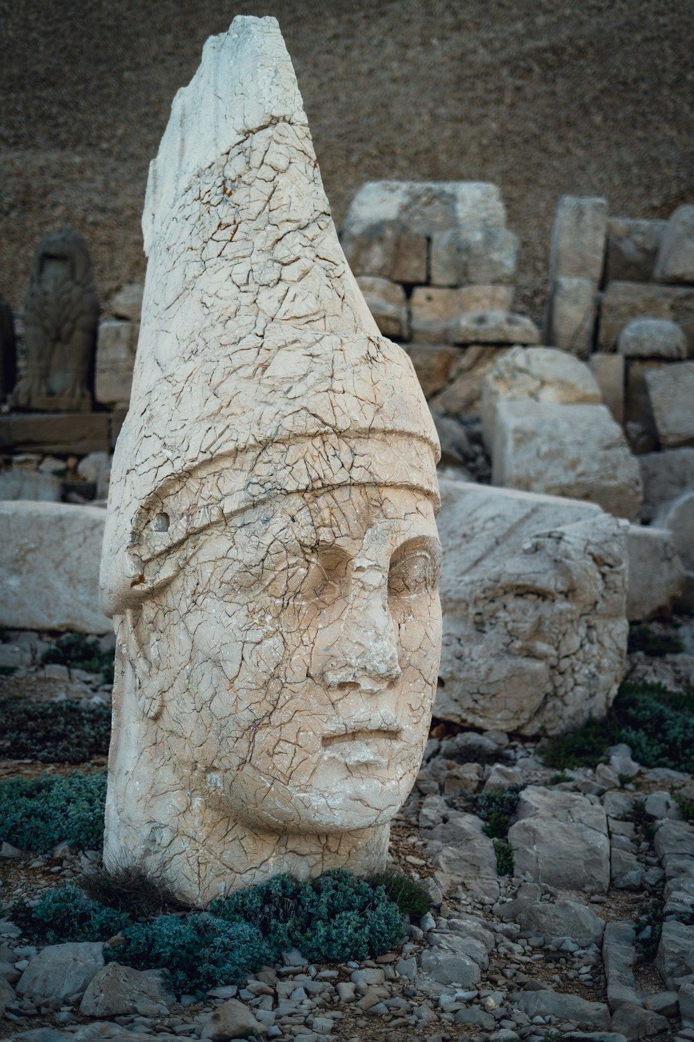a rock with a face carved into it with Mount Nemrut in the background
