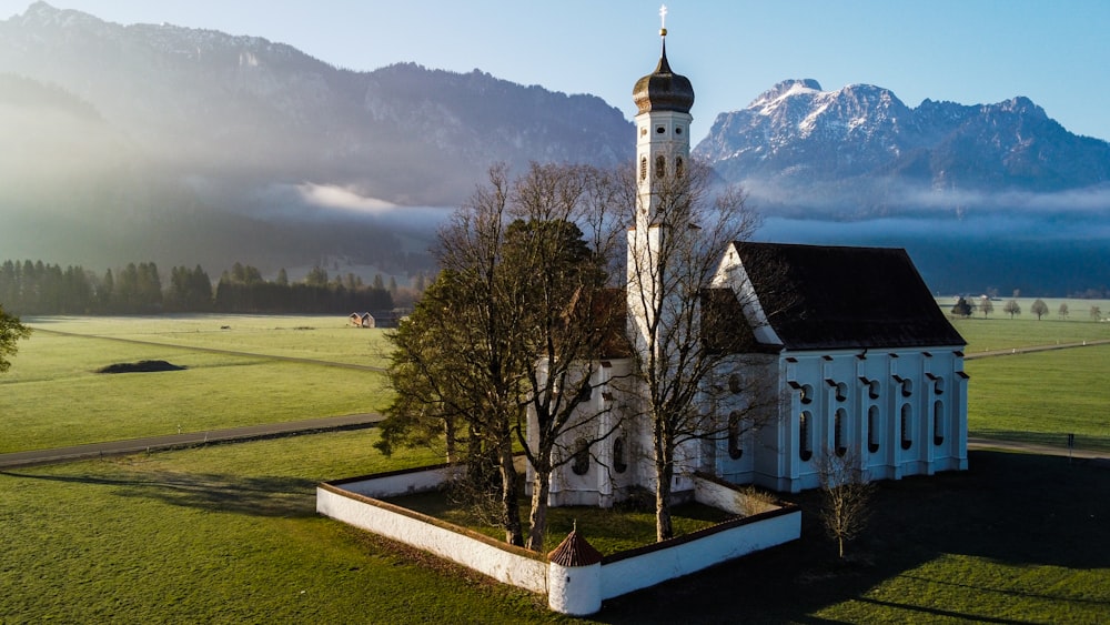 a building with a tower and a field with mountains in the background