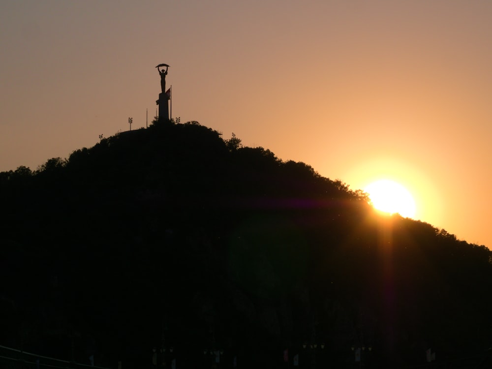 a silhouette of a tower on a hill with the sun setting