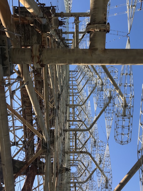 A large, complex metal structure with intricate latticed frameworks extending vertically into the sky. Several large metal beams and supports are interconnected, creating an industrial appearance.