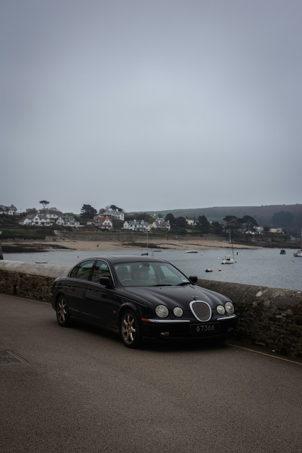 a black car parked on a road by water and boats