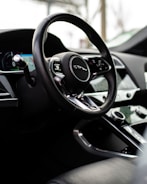 A close-up view of a car's interior, focusing on the steering wheel with a luxury logo. The dashboard features modern controls and a digital display. The surrounding environment suggests a sleek, high-quality design.
