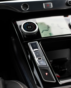 A close-up view of a car's center console featuring a digital temperature control knob set at 22 degrees, gear shift buttons labeled D, N, R, and P, and part of a touchscreen interface displaying seat and climate settings.