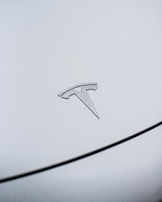 Close-up of a Tesla's illuminated electric blue logo against a polished navy blue body.
