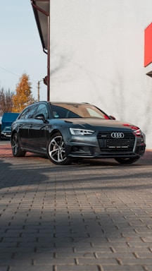A shiny silver Audi A4 parked in front of a modern building under bright sunlight.