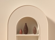 A set of elegant 3D printed vases displayed on a wooden shelf, showcasing subtle color gradients and delicate shapes.