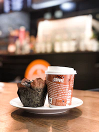 A steaming cup of coffee beside a plate of freshly baked muffins on a cozy cafe table.