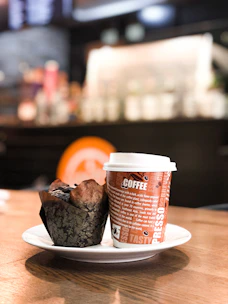 A steaming cup of coffee beside a plate of freshly baked muffins on a cozy cafe table.