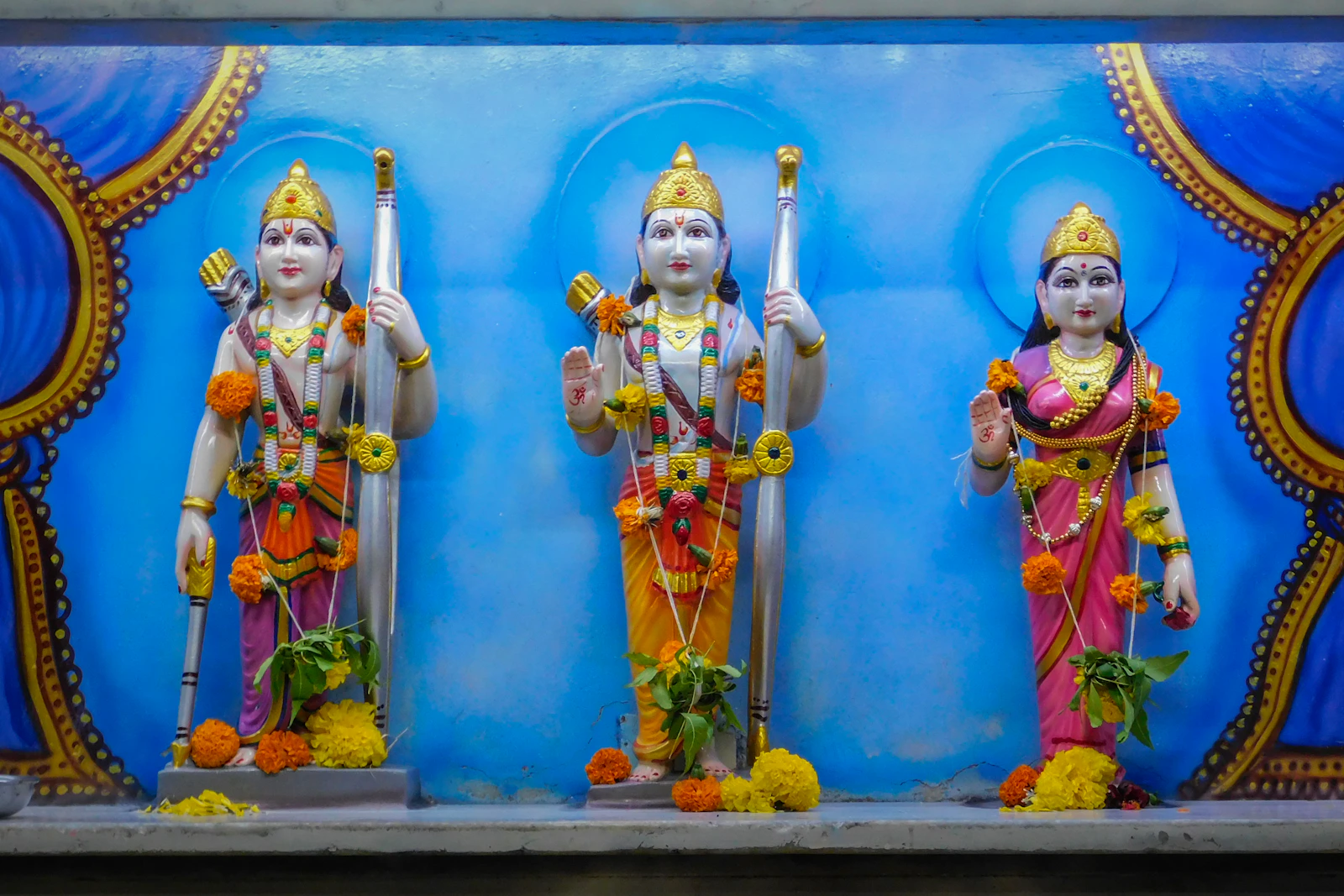 नीली पृष्ठभूमि पर राम, सीता और लक्ष्मण की प्रतिमाएं।