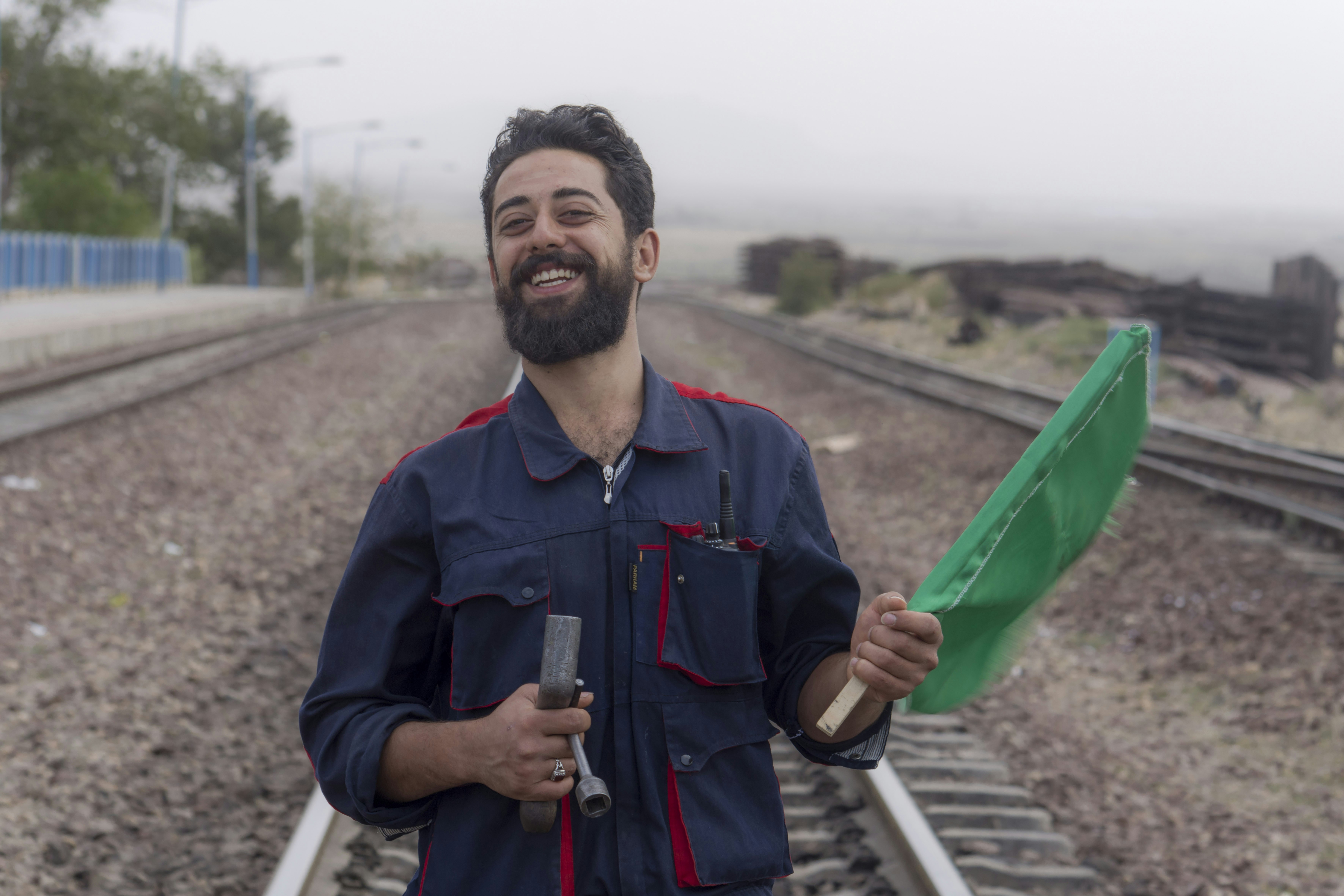 a man standing on a train track holding a green umbrella (Photo by Javad Esmaeili on Unsplash)