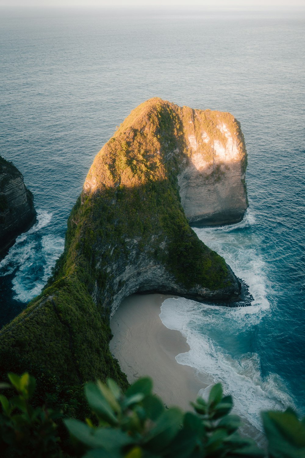 a large rock sticking out of the ocean next to a beach