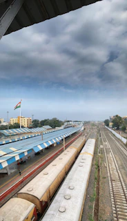 A bustling Indian railway station with passengers boarding a train under a bright summer sky.