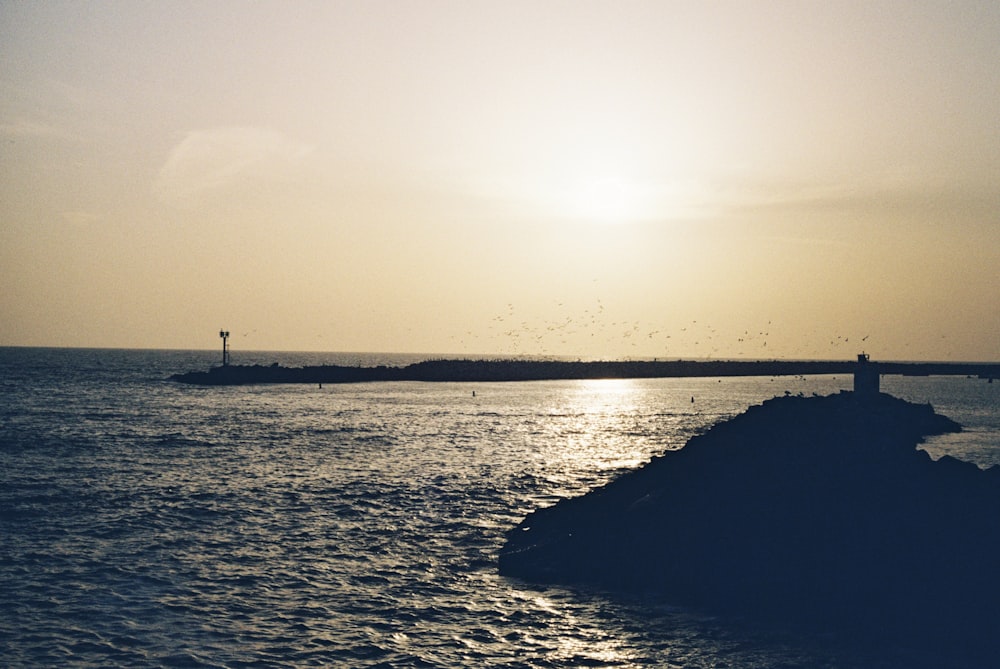 the sun is setting over the ocean with a lighthouse in the distance