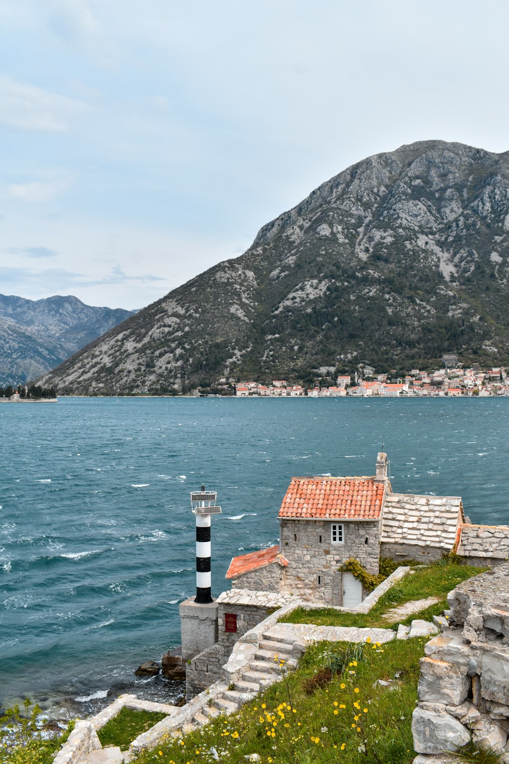 a lighthouse on the shore of a lake with mountains in the background