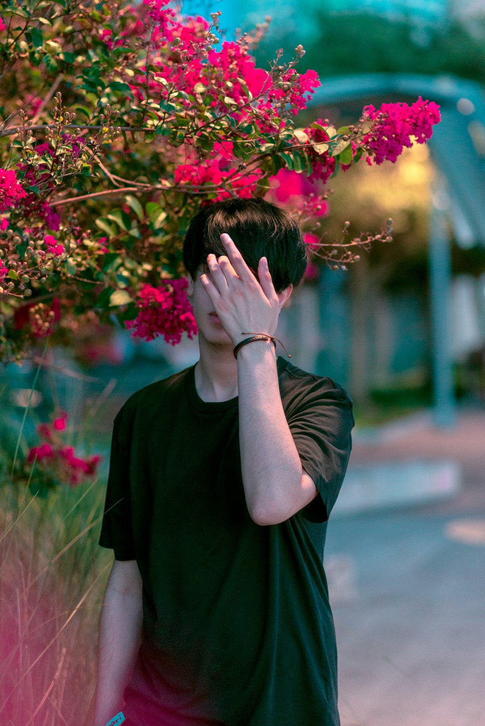 a man standing next to a bush with pink flowers