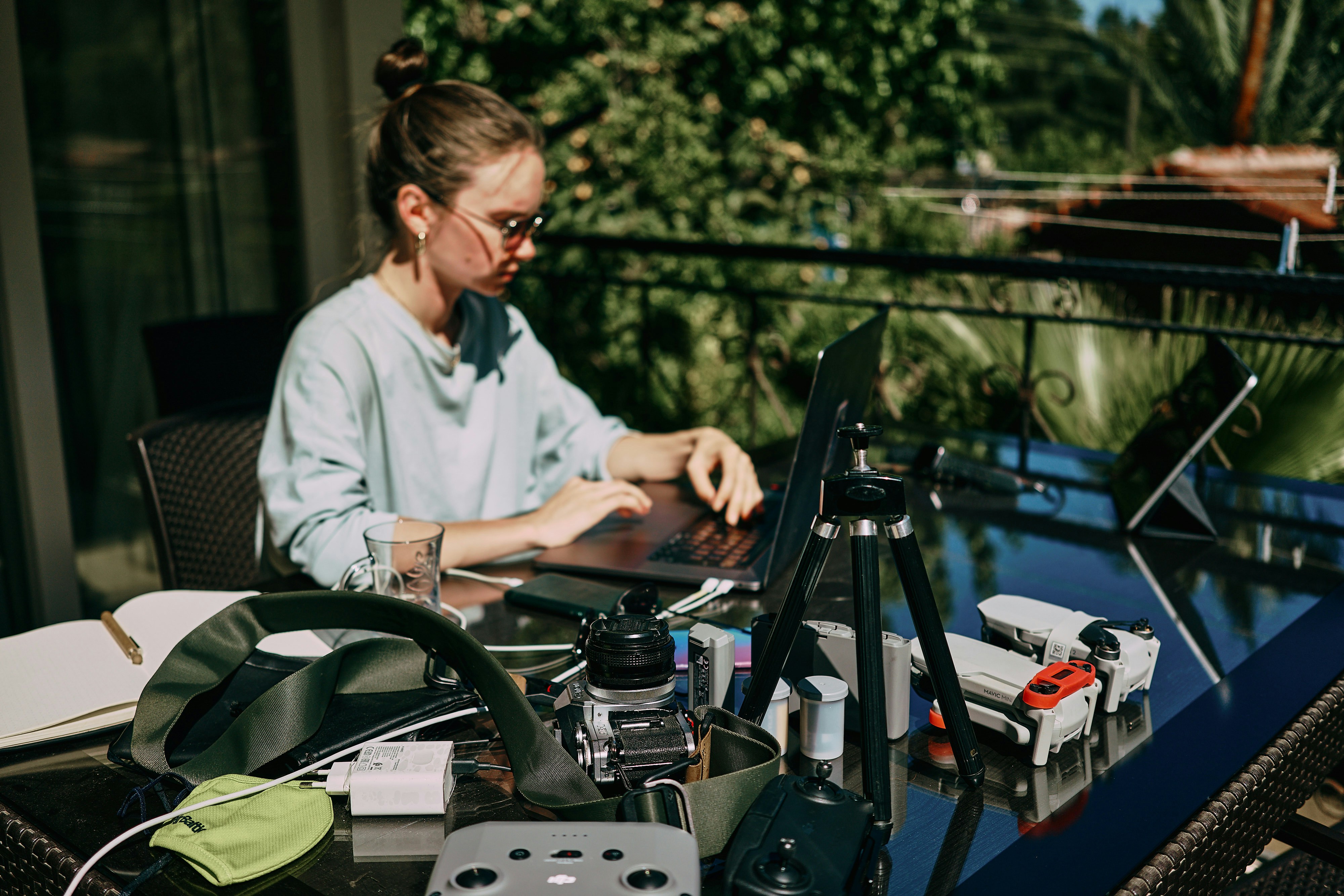 a woman sitting at a table with a laptop, A girl working on the table on the terrace. Many laptops and other staff. Side view