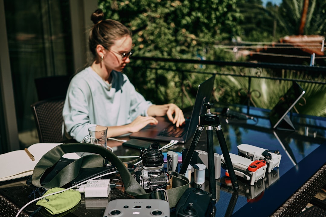 a woman sitting at a table with a laptop, A girl working on the table on the terrace. Many laptops and other staff. Side