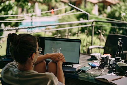 A gardener using a laptop outdoors with plants and landscaping tools around.