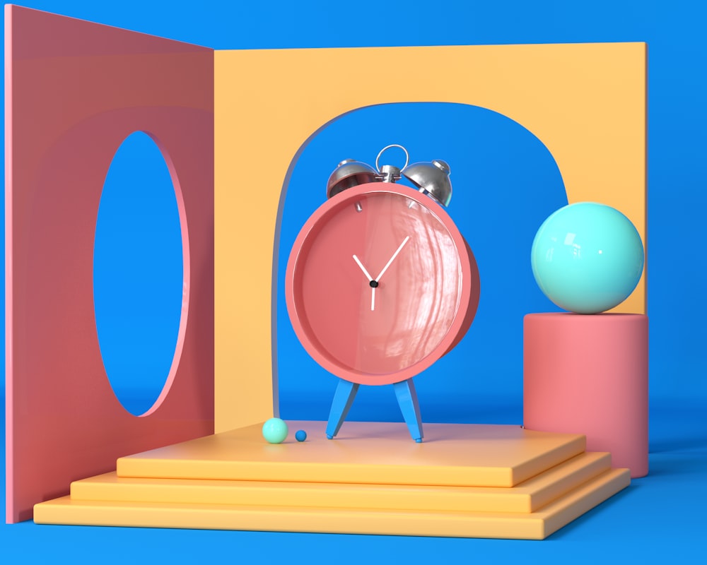 a pink clock sitting on top of a wooden block