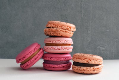 Close-up of pastel-colored macarons stacked in a neat pile on a soft cream background.