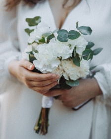 Beautifully manicured hands holding a bouquet of soft beige flowers in a warm light.