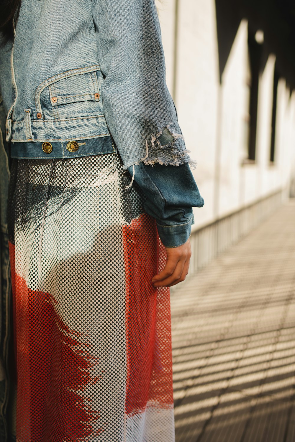 a woman wearing a jean jacket and a colorful skirt