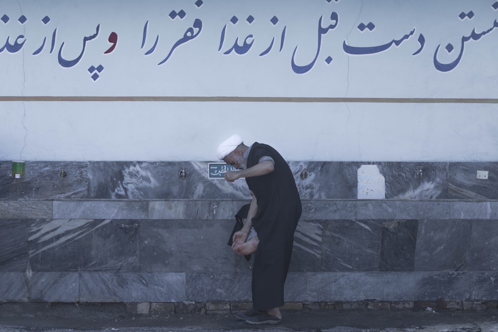 a man leaning against a wall with a cell phone in his hand