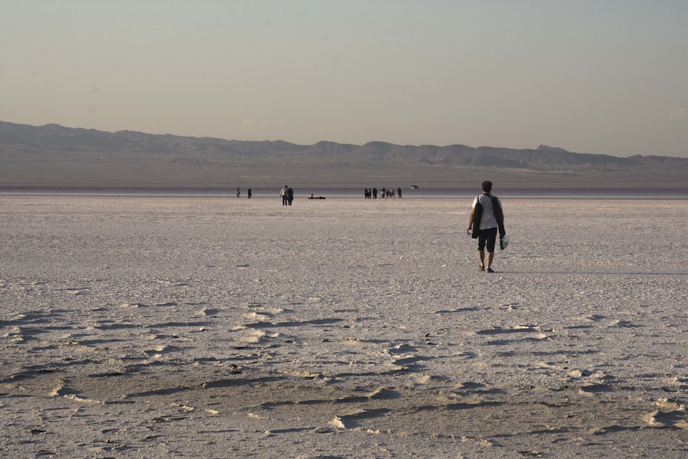 a man walking across a sandy beach next to mountains