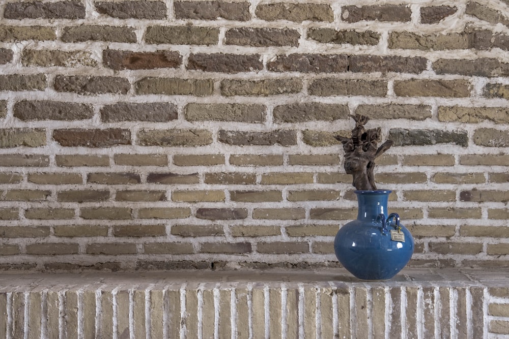 a blue vase sitting on a ledge in front of a brick wall