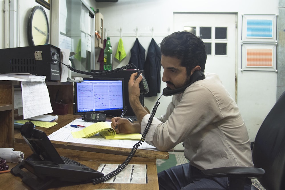 a man sitting at a desk talking on a phone