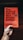 A hand holds a book titled 'The Subtle Art of Not Giving a F*ck' by Mark Manson. The cover is orange with black text, featuring a small black burst graphic and a circular sticker indicating it is a bestseller.