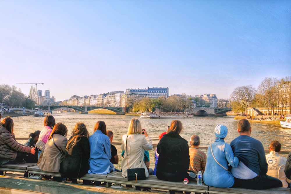 a group of people sitting on a bench next to a river