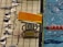 A starting block for swimming with the number 8, mounted poolside next to a lane divider. An orange cover is on the block and various flags are visible on the ground and hanging nearby. The block also has the brand name 'SEIKO' on it.