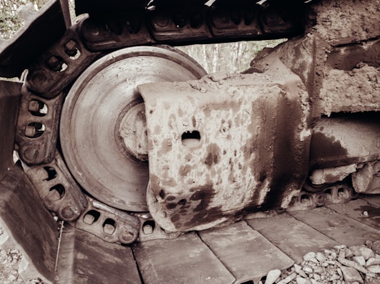 An up-close view of a large, dirt-covered metal track and wheel of heavy construction machinery. The mechanical parts are heavy-duty, showing wear and mud scattered over the surface.