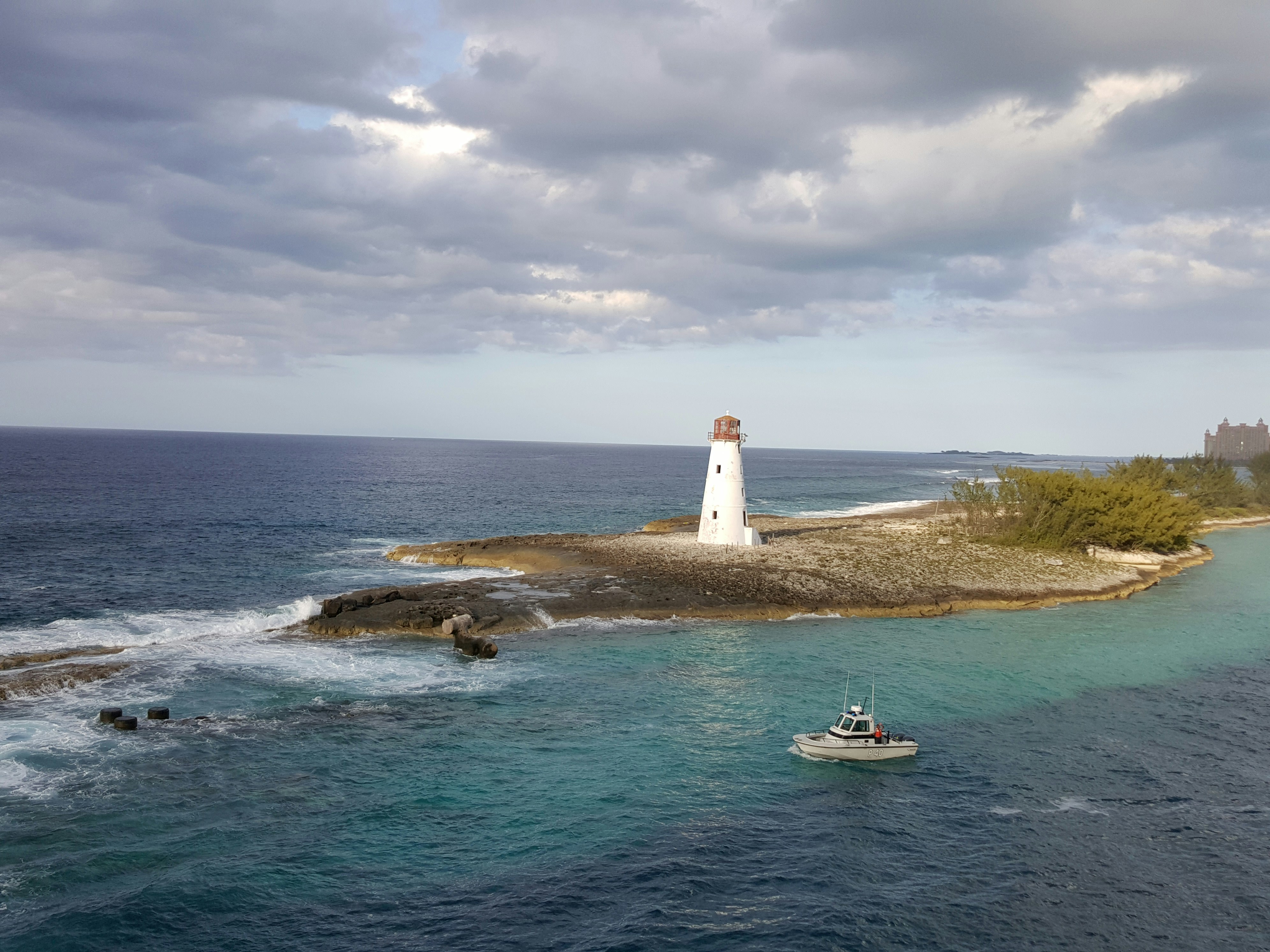 a small boat in the water near a light house, Entering harbor