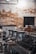 A commercial espresso machine with multiple portafilters and a row of cups on top, set against a background of a rustic, textured wall with a mix of exposed bricks and plaster.