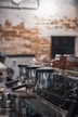 A commercial espresso machine with multiple portafilters and a row of cups on top, set against a background of a rustic, textured wall with a mix of exposed bricks and plaster.