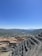 A large open-pit mine with terraced layers is visible in the foreground. Beyond the mine, a small town is nestled in a valley surrounded by lush green hills. The sky is clear and blue, suggesting a sunny day.