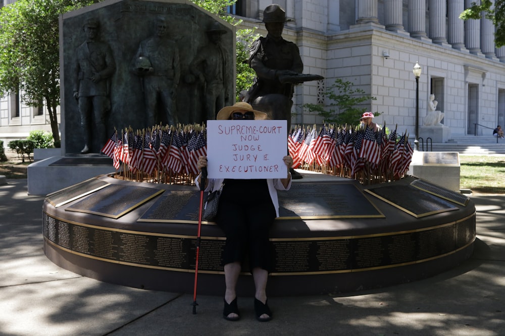 a woman holding a sign in front of a statue