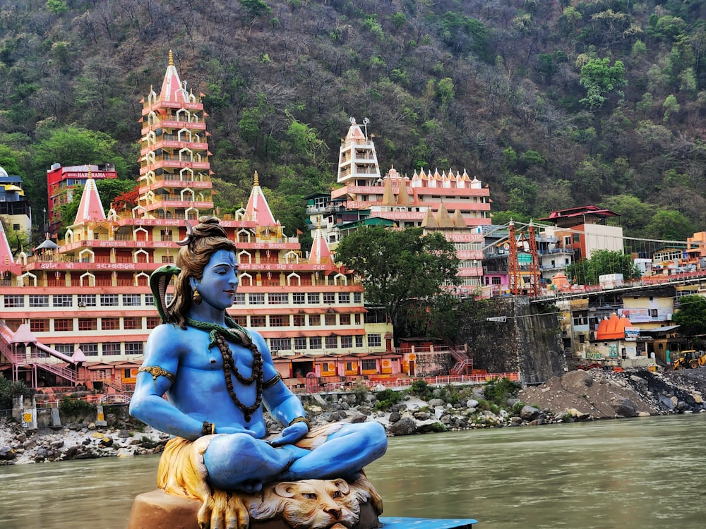 a statue of a person sitting on a rock in front of a body of water