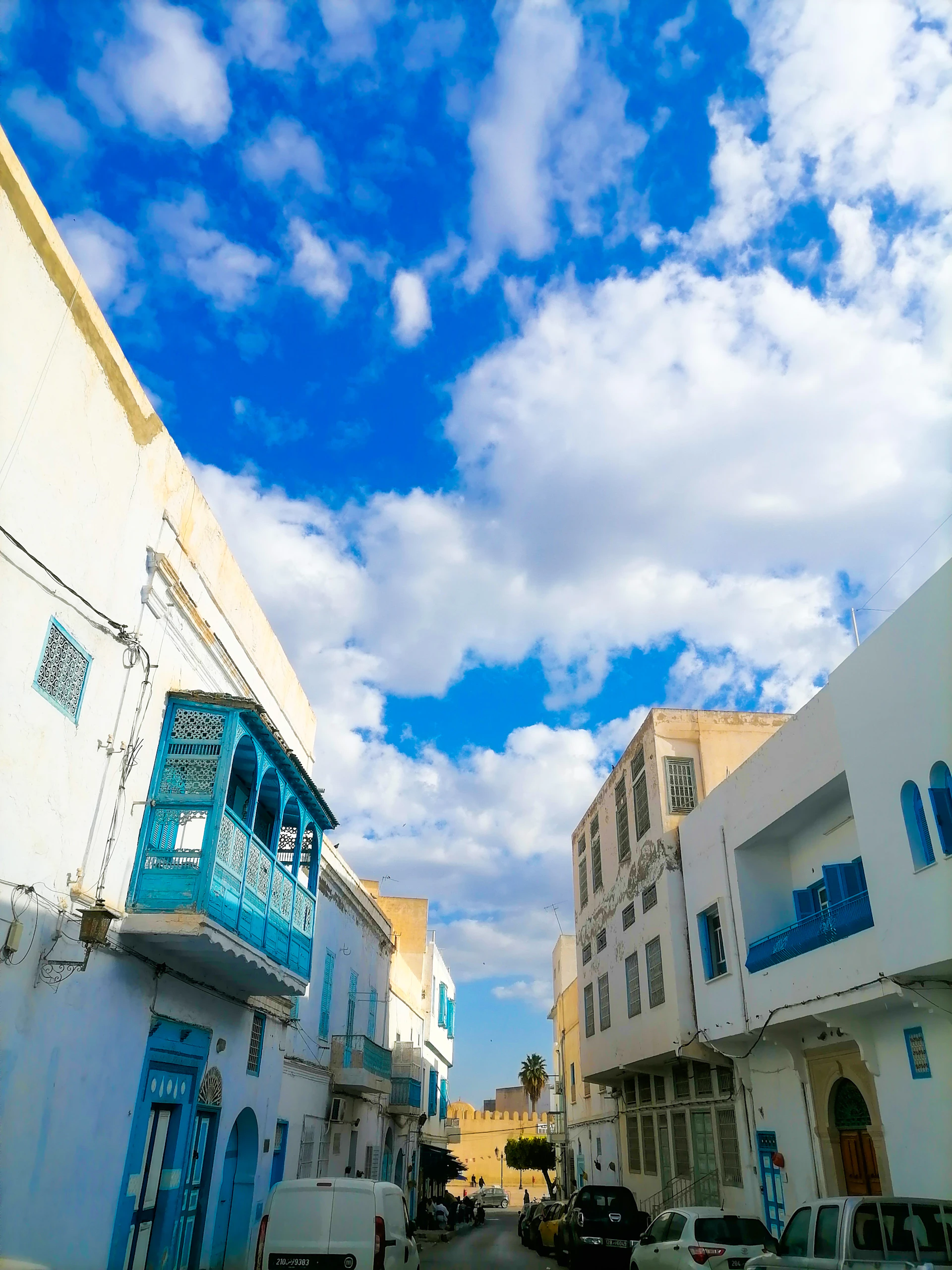 A vibrant street scene in Malta featuring colorful buildings and a glimpse of the Mediterranean Sea under a clear blue sky.