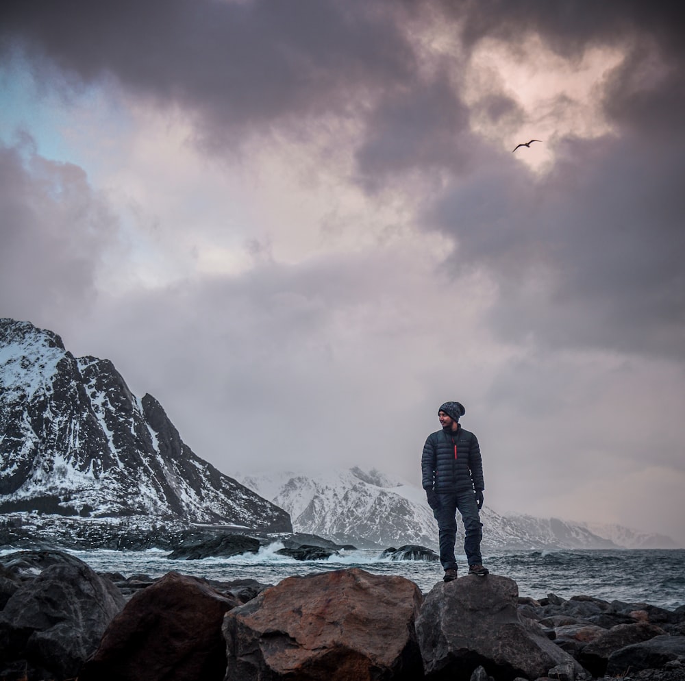 a man standing on a rocky beach next to a mountain