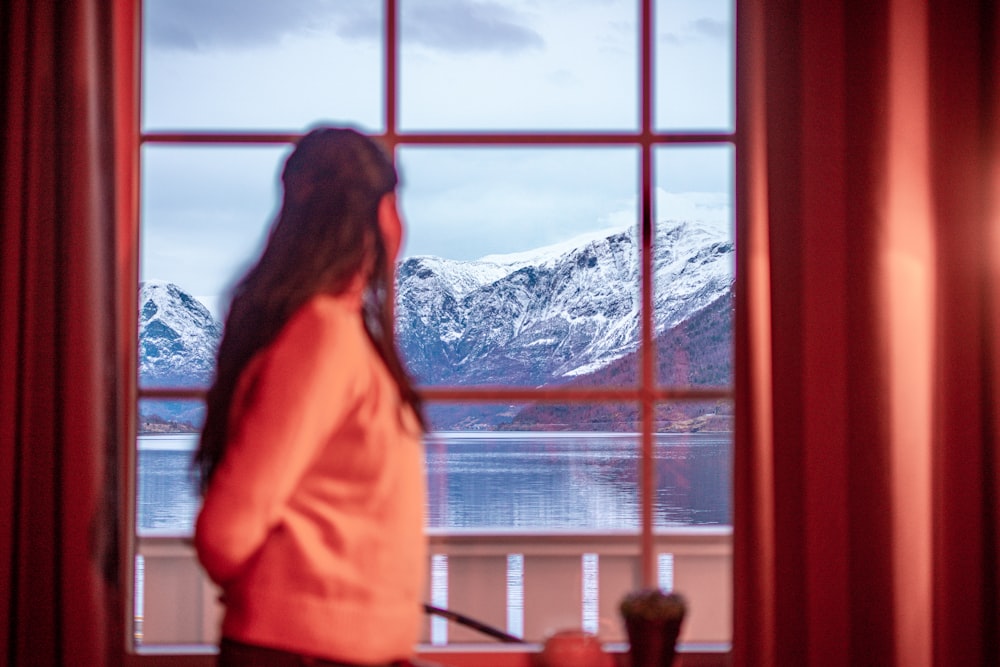 a woman standing in front of a window looking out at mountains