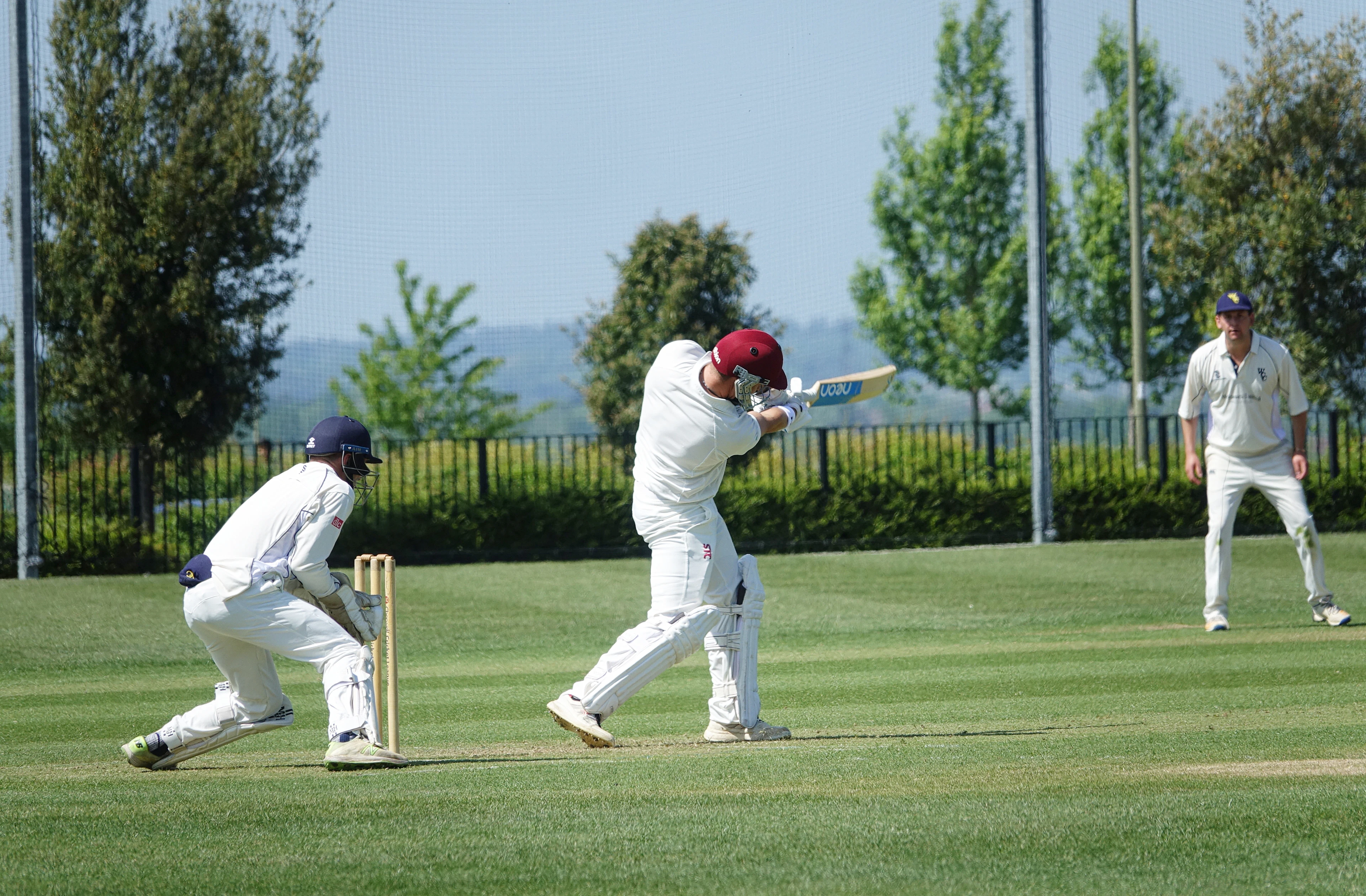 Club cricketer cutting the ball as the wicketkeeper crouches behind the stumps on a sunny afternoon