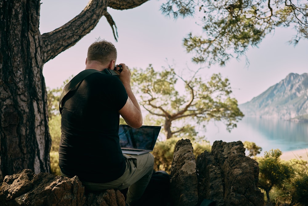 a man sitting on top of a rock next to a tree