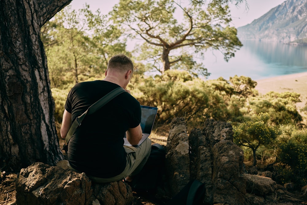 a man sitting on top of a rock next to a tree